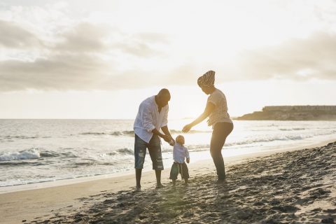 African american toddler with parents at sunset on the beach - Black family enjoy summer vacation - Mother, father and child love