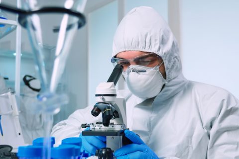 Biotechnology scientist in ppe suit researching DNA in laboratory using microscope. team examining virus evolution using high tech for scientific research of vaccine development against covid19